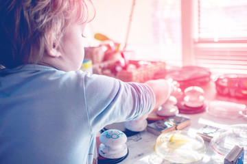 boy is having fun while playing with stamps and tempera paints on wooden work desk producting...