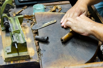 Traditional manufacture of cigars at the tobacco factory. Closeup of old hands making a cigar from tobacco leaves in a traditional cigar manufacture. Close up hands making a cigar from tobacco leaves