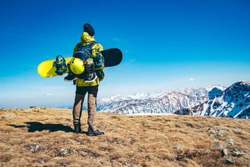 A man standing on the top of a mountain with snowboarding gear strapped to his backpack