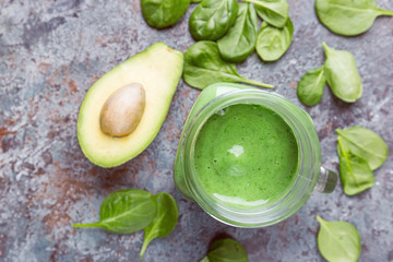 Healthy green smoothie with spinach, avocado, banana and chia seeds in glass jars on gray stone background, top view.