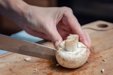 Girl cook is cutting mushrooms on a wooden Board