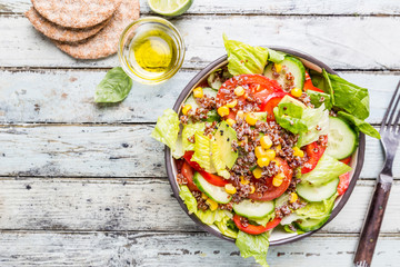 Fresh healthy salad with quinoa, red tomatoes, sweet pepper, cucumber, corn and avocado on white wooden background, top view. Healthy food. Superfood meal.