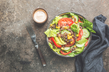 Fresh healthy salad with quinoa, red tomatoes, sweet pepper, cucumber, corn and avocado on stone background, top view. Healthy food. Superfood meal.