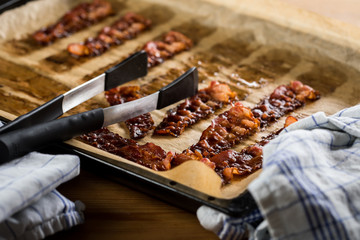 Knusprig gebratene Bacon Speck Scheiben aus dem Ofen auf Backblech mit Backpapier mit Geschirrtuch und Zange in Küche