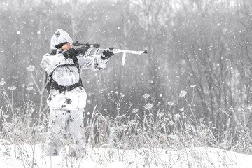 Man soldier in the winter on a hunt with a sniper rifle in white winter camouflage aiming standing in the snow