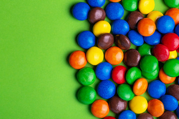 Fototapeta na wymiar Glazed colored chocolate candies are gathered on bright green background