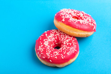 Two delicious pink donuts with sprinkle on bright blue background