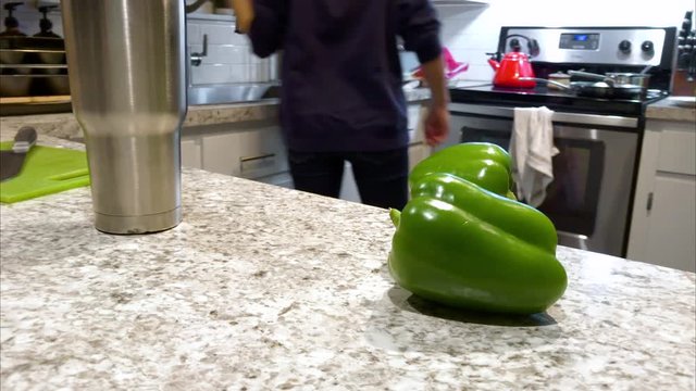 Focus on bell peppers while woman cooks in kitchen