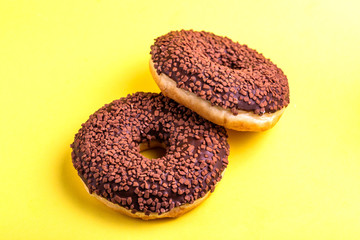 Two delicious chocolate donuts with sprinkle on bright yellow background