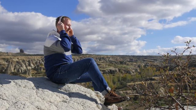 man listening to music in headphones sitting on a rock in cappadocia