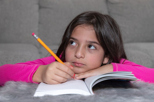 A young girl holding a yellow pencil is thinking while doing her homework