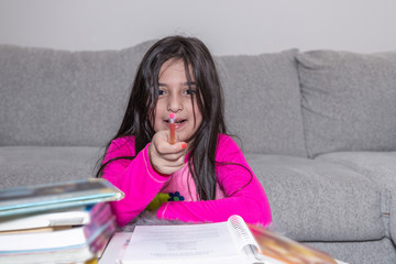 A young girl doing her homework is pointing the pencil