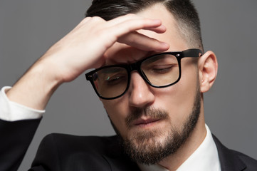 Close-up Serious businessman in formal suit and glasses posing on gray background.