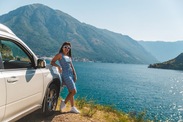 woman standing on cliff near white suv car with beautiful view of sea bay with mountains