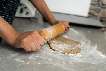 Two hands rolling, the biscuit dough evenly over flour with a rolling pin, making cookies and gingerbread in the kitchen