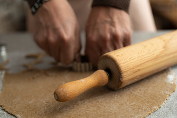close up of a rolling pin and hands who are cutting out cookies of the biscuit dough