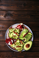 sliced avocado and ripe pomegranates on toast bread with spices and avocado.