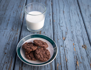 A cup of milk and plate of cookies on blue wooden floor