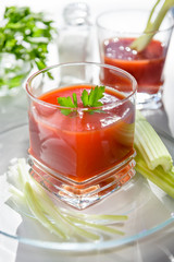 Fresh tomato juice. Most useful juice. Tomato juice is poured into a transparent glass with parsley and herring, on a white background, illuminated by sunlight.