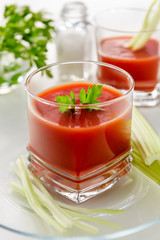Fresh tomato juice. Tomato juice is poured into a transparent glass with parsley and herring, on a white background, illuminated by sunlight.