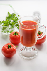 Tomato juice is poured into a transparent glass with parsley and herring, on a white background with cherry tomatoes, lit by sunlight. The most useful juice. Tomato juice from fresh tomatoes.