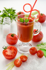 Tomato juice in glass with celery, cherry tomato, white wood background, closeup. Tomato juice from fresh tomatoes.