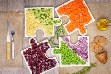 Assemble jigsaw puzzles for healthy. Delicious fresh pieces of vegetables of carrots, cucumber, potatoes, beets and peas close-up with fresh onion and olive oil on a bag cloth on a rustic gray table.