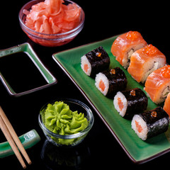 Japanese rolls with spicy wasabi. Japanese food. Set of various rolls of salmon, eel, shrimp and red caviar, in a beautiful green bowl, on a black background with reflection.