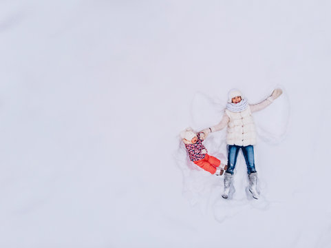 Snow angel shows. Mom and daughter lie in drift, making figures, waving their hands like bird. View top