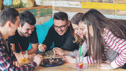 Happy friends sharing slice of cake at restaurant - Friendship concept with young people enjoying time together and having genuine fun at rustic cafe eating chocolate cake - Focus on guy with glasses - 243193200