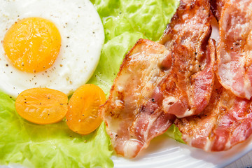 Fried bacon. Morning breakfast with delicious fried bacon, French fries and tender egg, close-up.