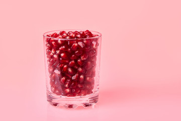 Close-up of pomegranate seeds in a glass on a pink background, top view.  Ripe red garnet fruit. Pomegranate juice in a glass. Fresh Garnet