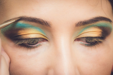Naklejka premium Professional makeup artist applying makeup for young woman in studio. Makeup detail.