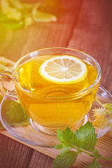 A cup of tea with fragrant tea, standing on a wooden table, in the rays of sunlight.