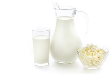 Cow milk in a glass jug and cup in a next to a plate of fresh cottage cheese on white background....
