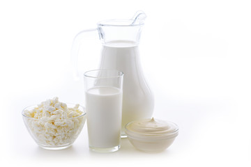 Cow milk in a glass jug and cup in a next to a plate of fresh cottage cheese on white background. Healthy food for people. Dairy kitchen is very useful for bone health.