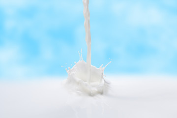 Milk splash of pouring milk against the blue sky. Frozen instant of milky splash.Milk background of frozen splash.
