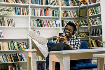 Happy and fun african american hipster boy sitting at the library table and dancing waving his hands