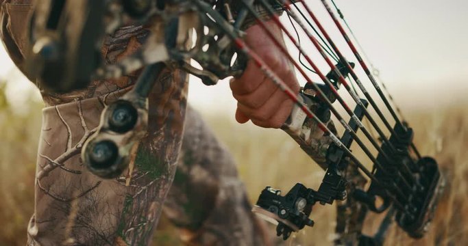 Close up shot of bowhunter's hand carrying a compound bow and arrows while he walks