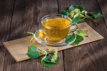 Tea with linden and lemon. Cup with fragrant lime tea, standing on a wooden table, in the rays of sunlight.