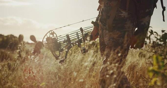 Bowhunter's legs and torso walking through golden prairie grass and exiting frame