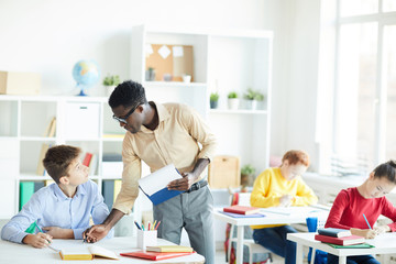 Fototapeta premium Clever schoolboy and his teacher looking at one another at lesson while discussing notes in copybook
