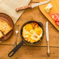 Rural scrambled eggs with tomatoes and onions in a cast iron pan on a rustic wooden table