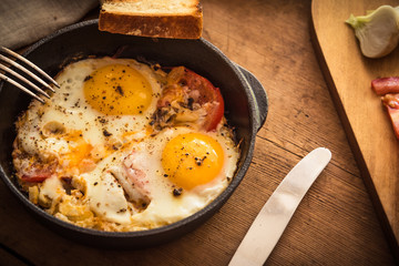 Rural scrambled eggs with tomatoes and onions in a cast iron pan on a rustic wooden table