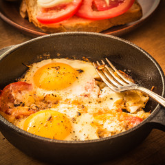 Rural scrambled eggs with tomatoes and onions in a cast iron pan on a rustic wooden table