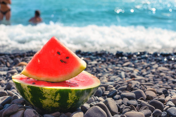 A large, juicy, cut watermelon, lies on a pebble beach on the shore of the blue sea.