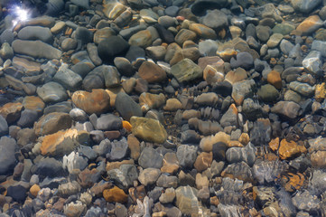 Stones lying in the water. Blue sea water splash. Background of sea water. Natural stone closeup background. Stone pattern.
