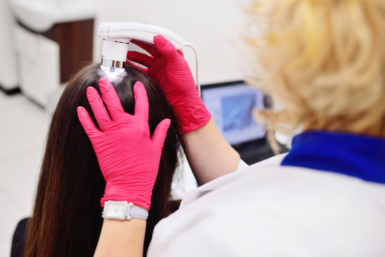 doctor dermatologist diagnoses the structure of the hair of a young pretty girl with a special tool - a trichoscope. Trichology, trichogram
