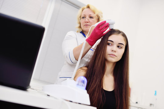 doctor dermatologist diagnoses the structure of the hair of a young pretty girl with a special tool - a trichoscope. Trichology, trichogram