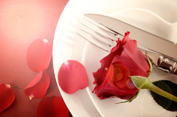 Happy Valentine's Day table place setting on red vintage wood background with red rose, overhead with lens flare.